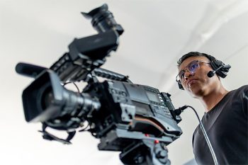 Male cameraman wearing headset, operating a camera for television broadcasting
